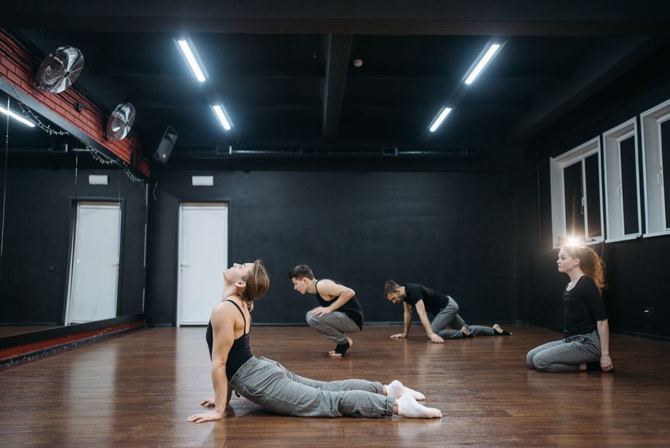 A group of dancers practicing in a contemporary dance studio with hardwood floors.