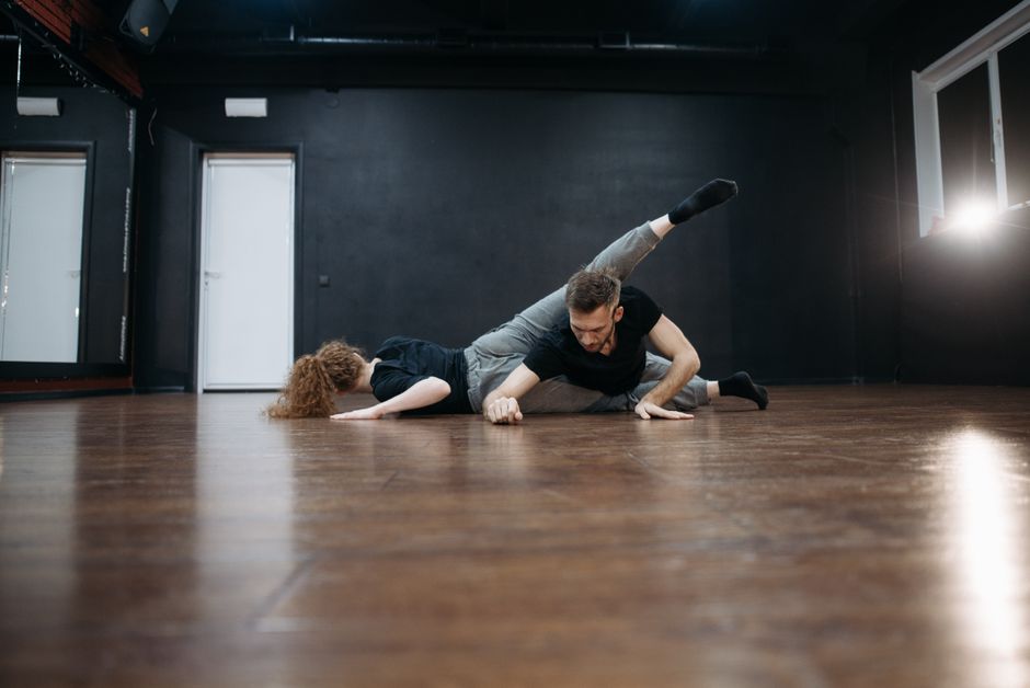 Male and female dancers performing a contemporary routine on a wooden floor in a studio.