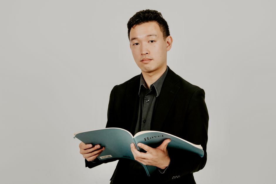 A musician in formal attire holding a music score book, looking confident.