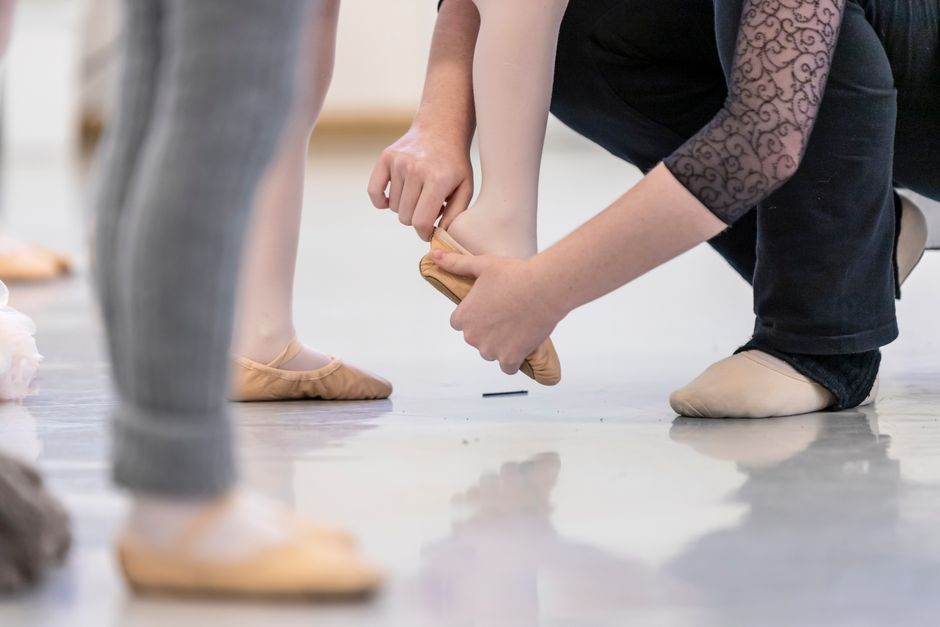 A close-up view of a ballet instructor adjusting a pointe shoe for a young dancer during training.